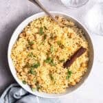 A plate of chickpea rice served with spoon with 2 glasses of water in the background.