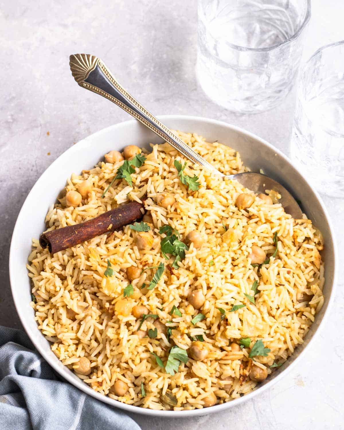 A plate of chickpea and rice served with a spoon with a glass of water in the background.