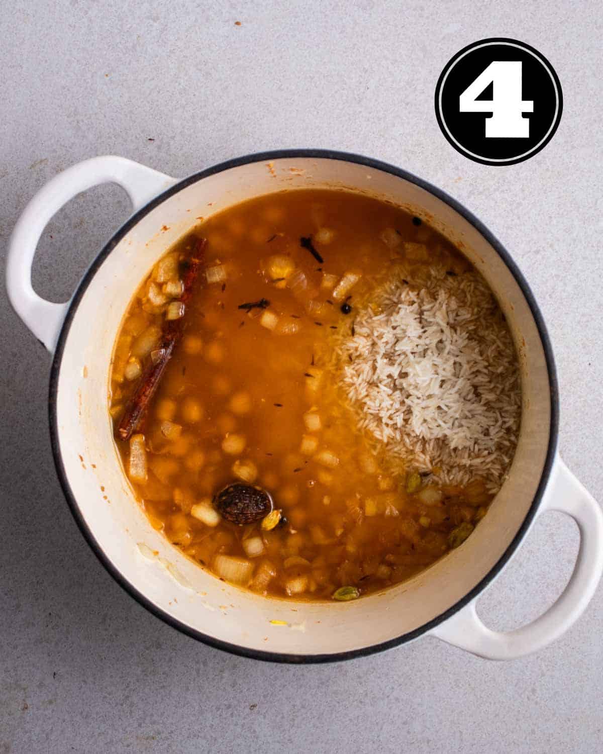 Uncooked rice and chickpeas in broth in a white Dutch oven.