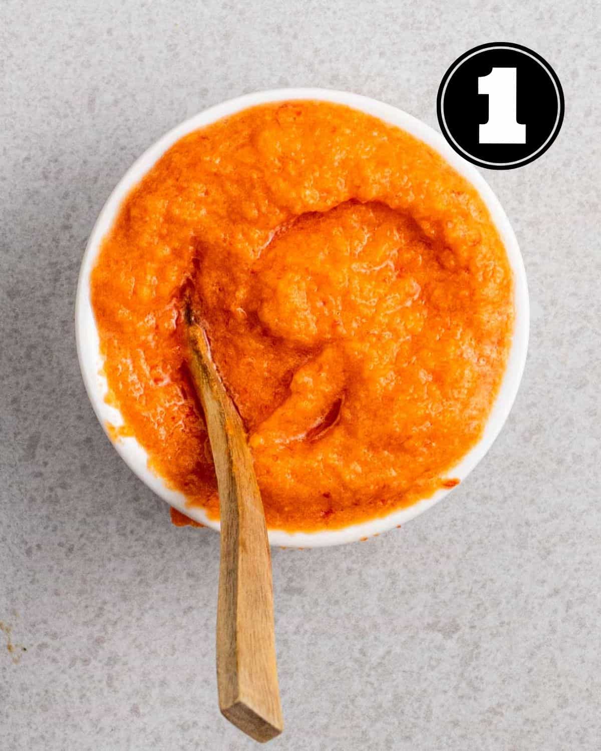 Chili paste in a ramekin with a wooden spoon beside.