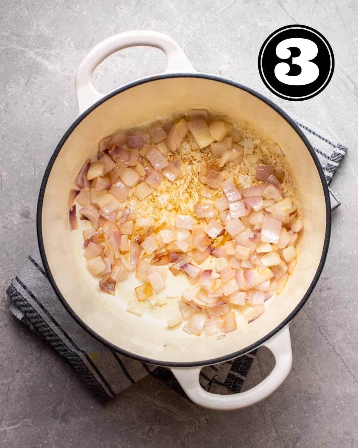Cooked onion in a white Dutch oven on a blue striped folded teacloth.