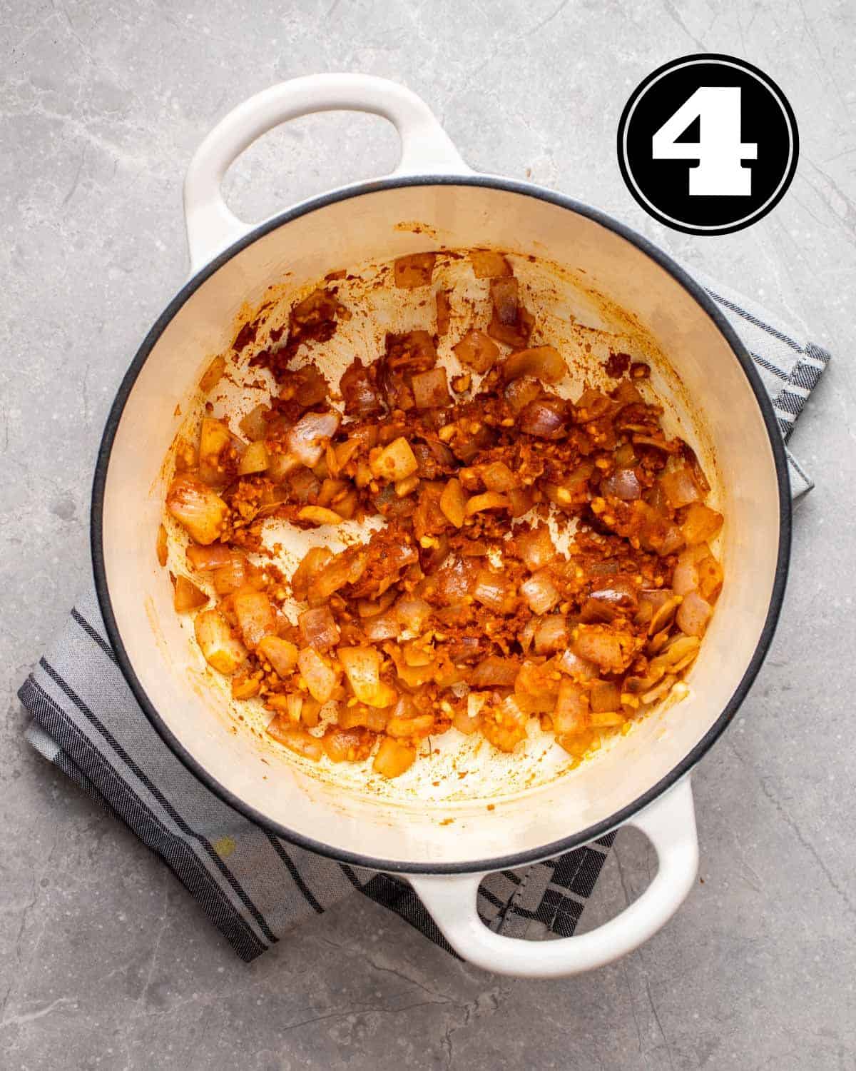 Fried red curry paste, onion, ginger, and garlic in a white Dutch oven.
