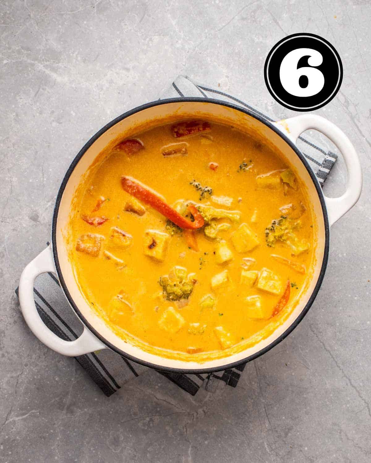 A pot of tofu red curry on a blue striped teacloth.