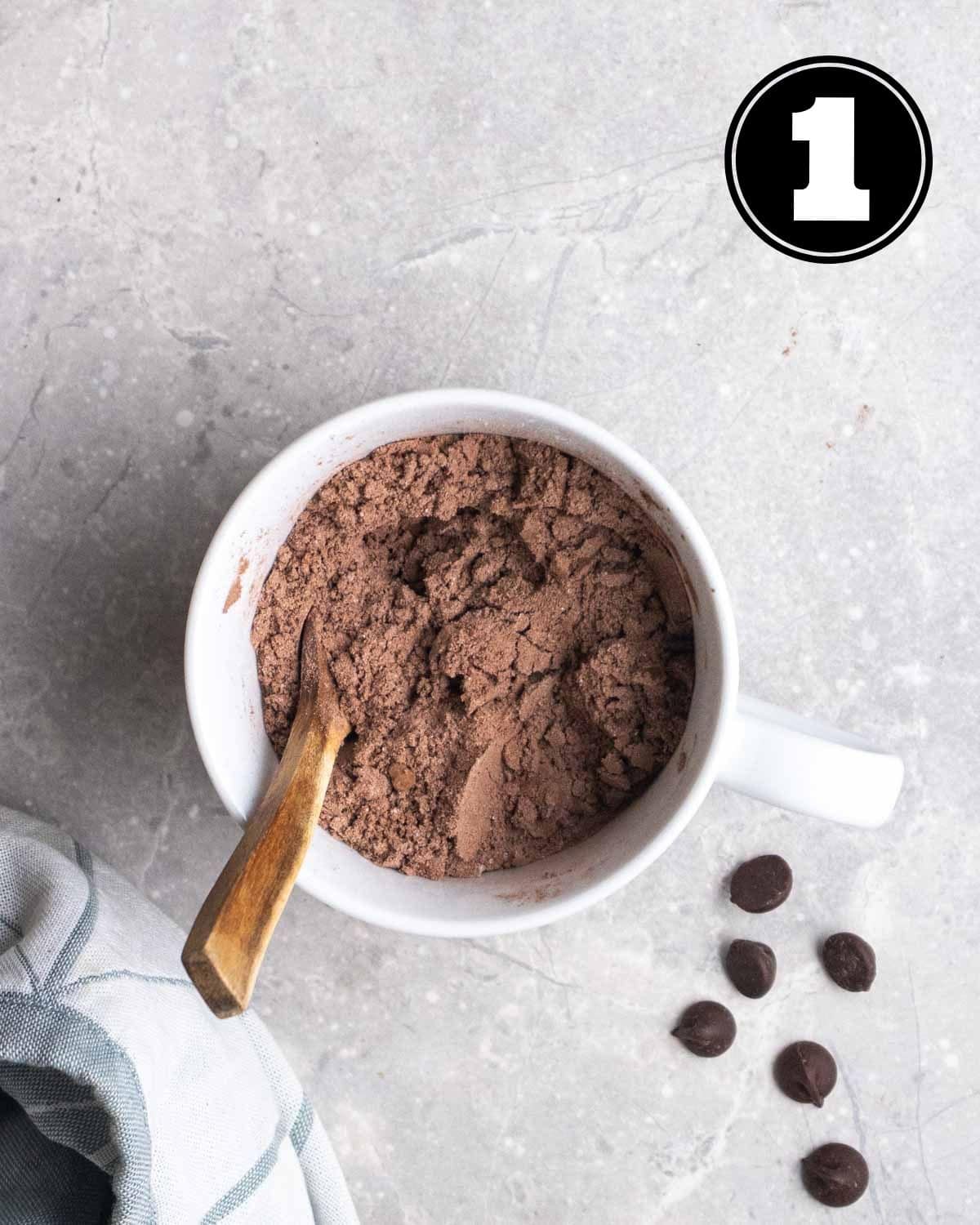 Dry ingredients in a mug with a wooden spoon beside.