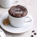 Protein mug cake topped with icing sugar served on saucer with a teaspoon beside.