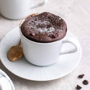 Protein mug cake topped with icing sugar served on saucer with a teaspoon beside.