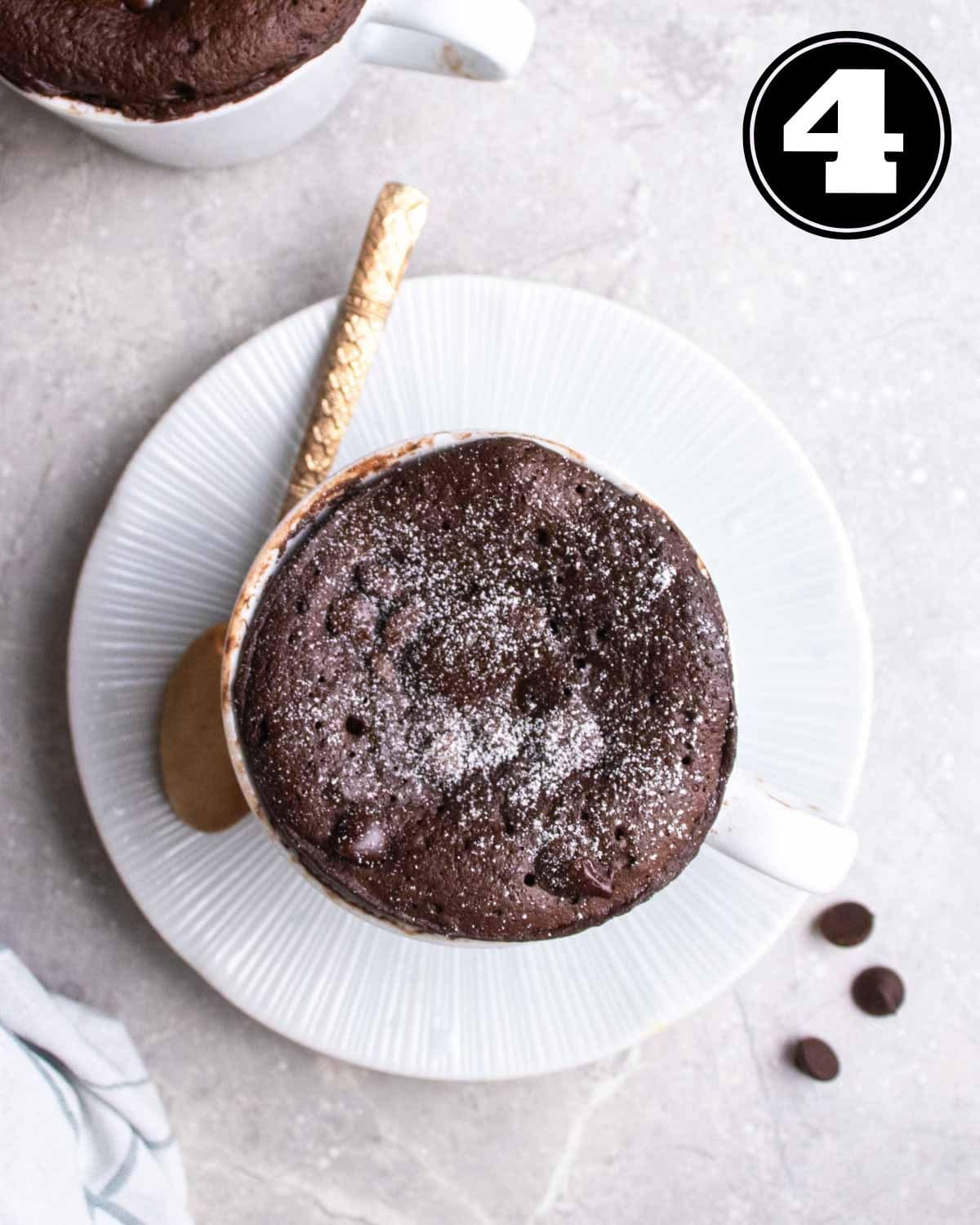 A protein mug cake served on a saucer with a teaspoon beside.