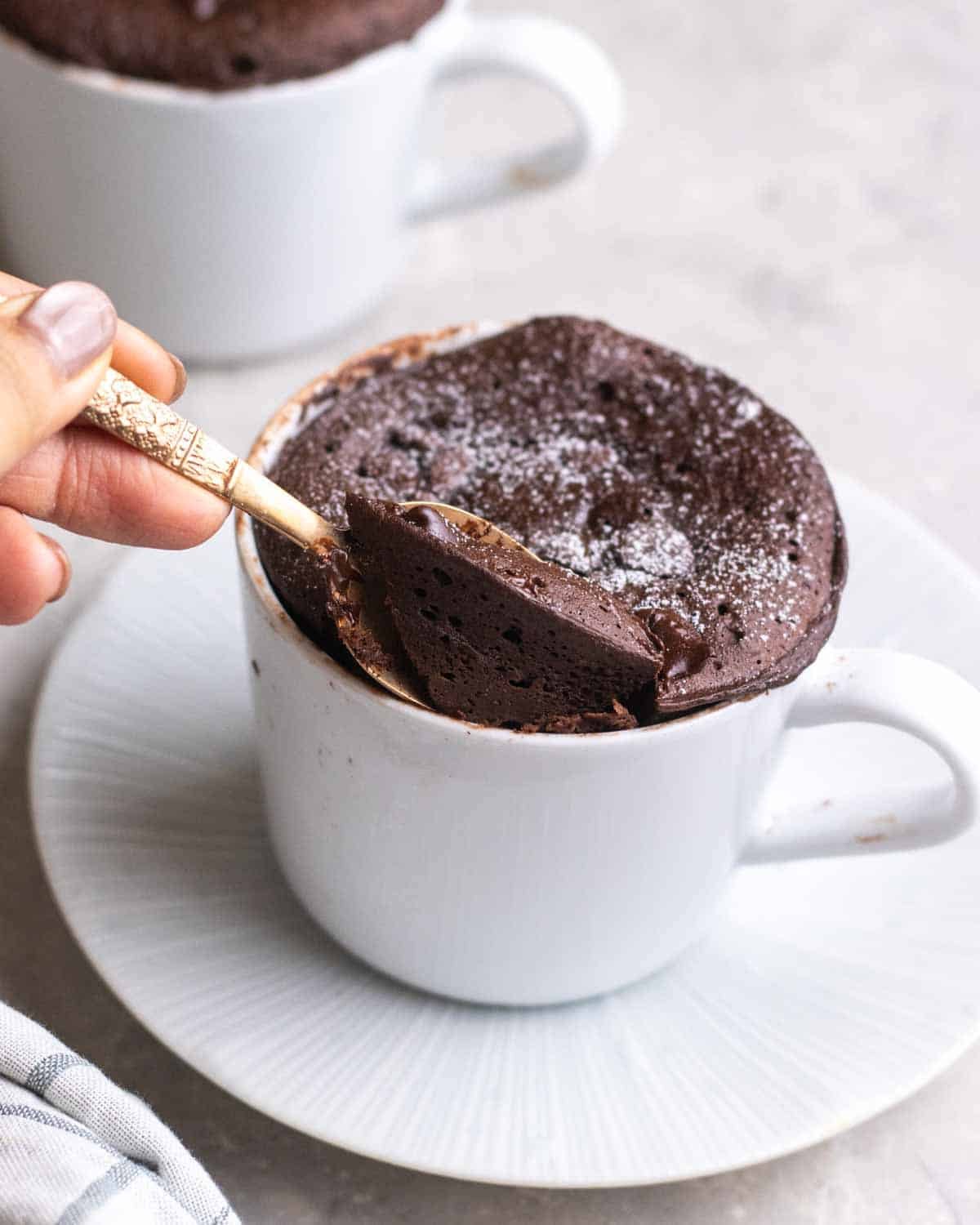 Spooning out a bite of chocolate protein mug cake on a saucer.