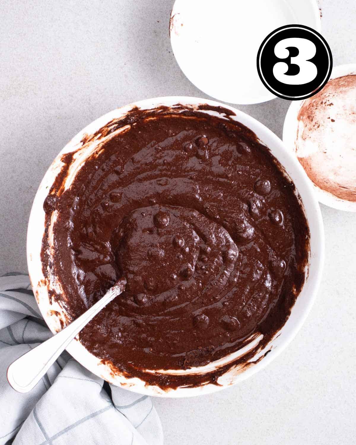 Brownie batter in a bowl with a spoon beside.